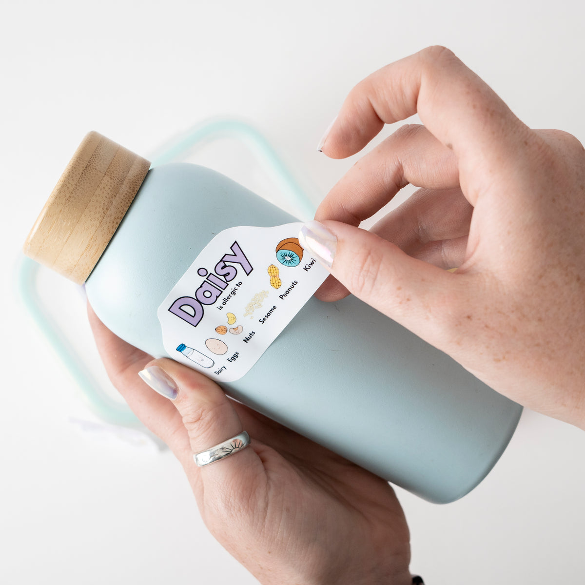 Hand holding a bottle labeled 'Daisy' with a white background