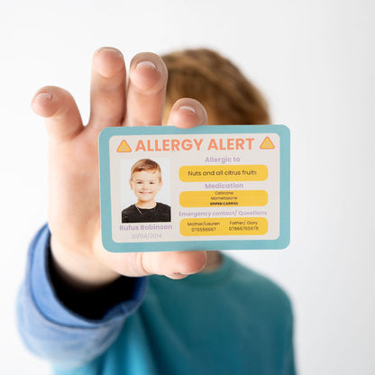Hand holding a allergy alert card with a child's photo and information on a white background