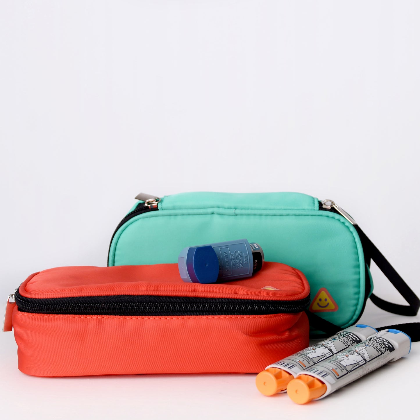 Two bags, one red and one green, with EpiPens and inhalers on a white background