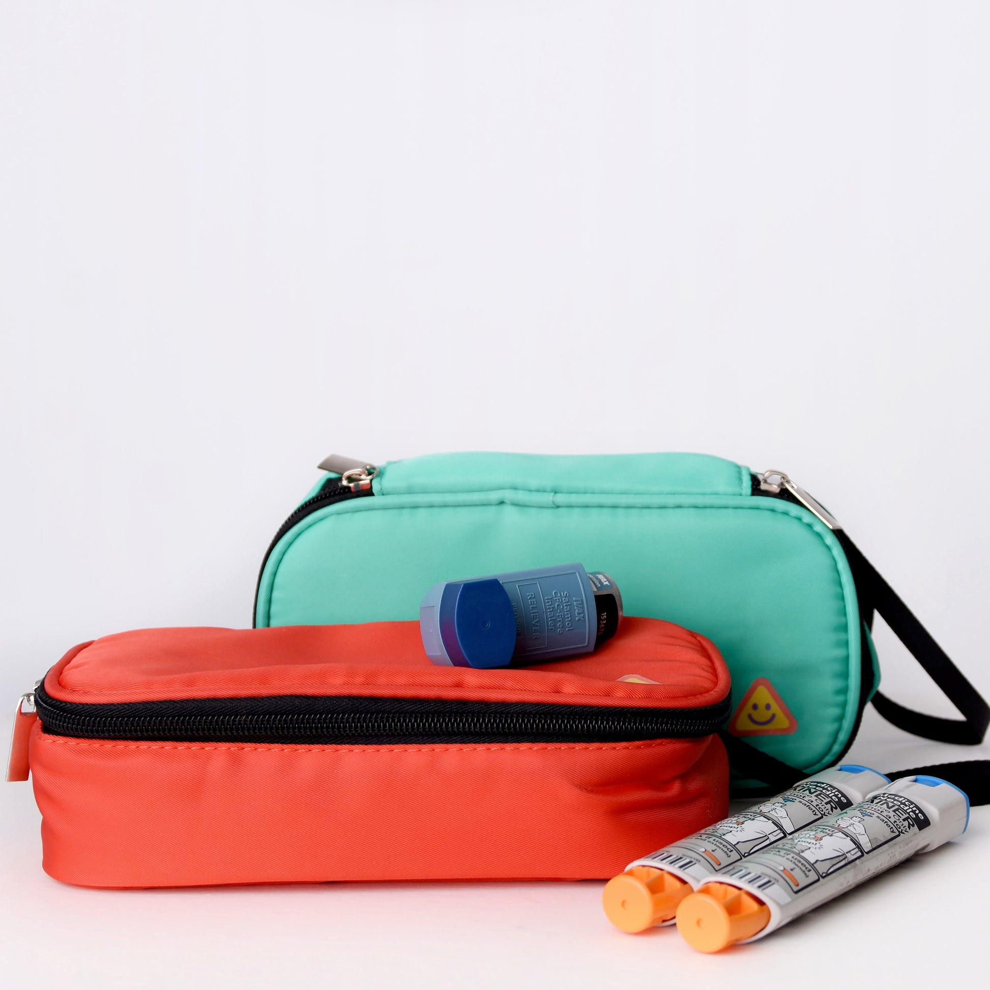 Two bags, one red and one green, with EpiPens and inhalers on a white background