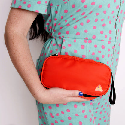Person wearing a teal dress with pink polka dots holding an orange allergy travel pouch.