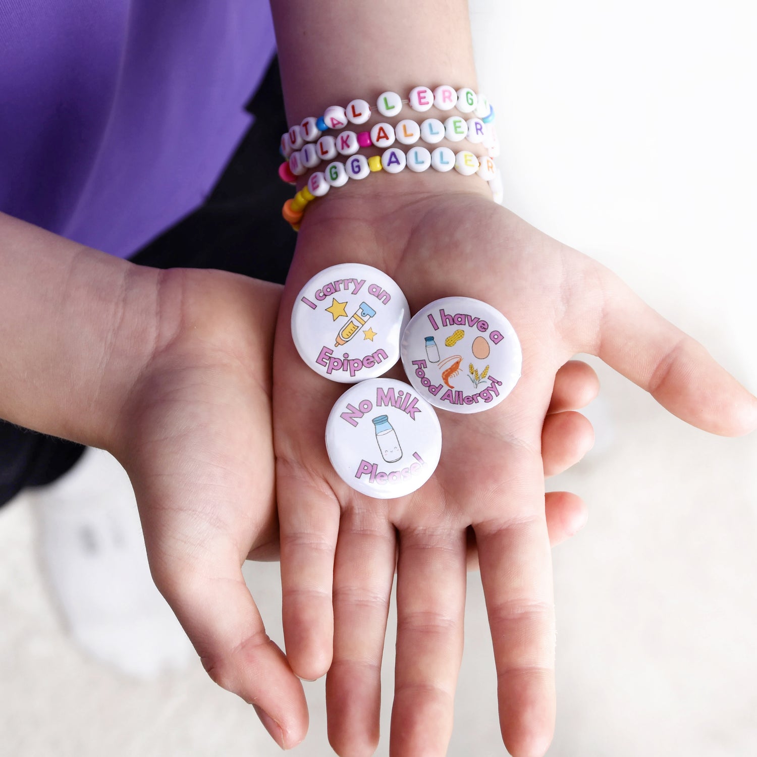 Hands wearing colourful bracelets with round badges on a white background