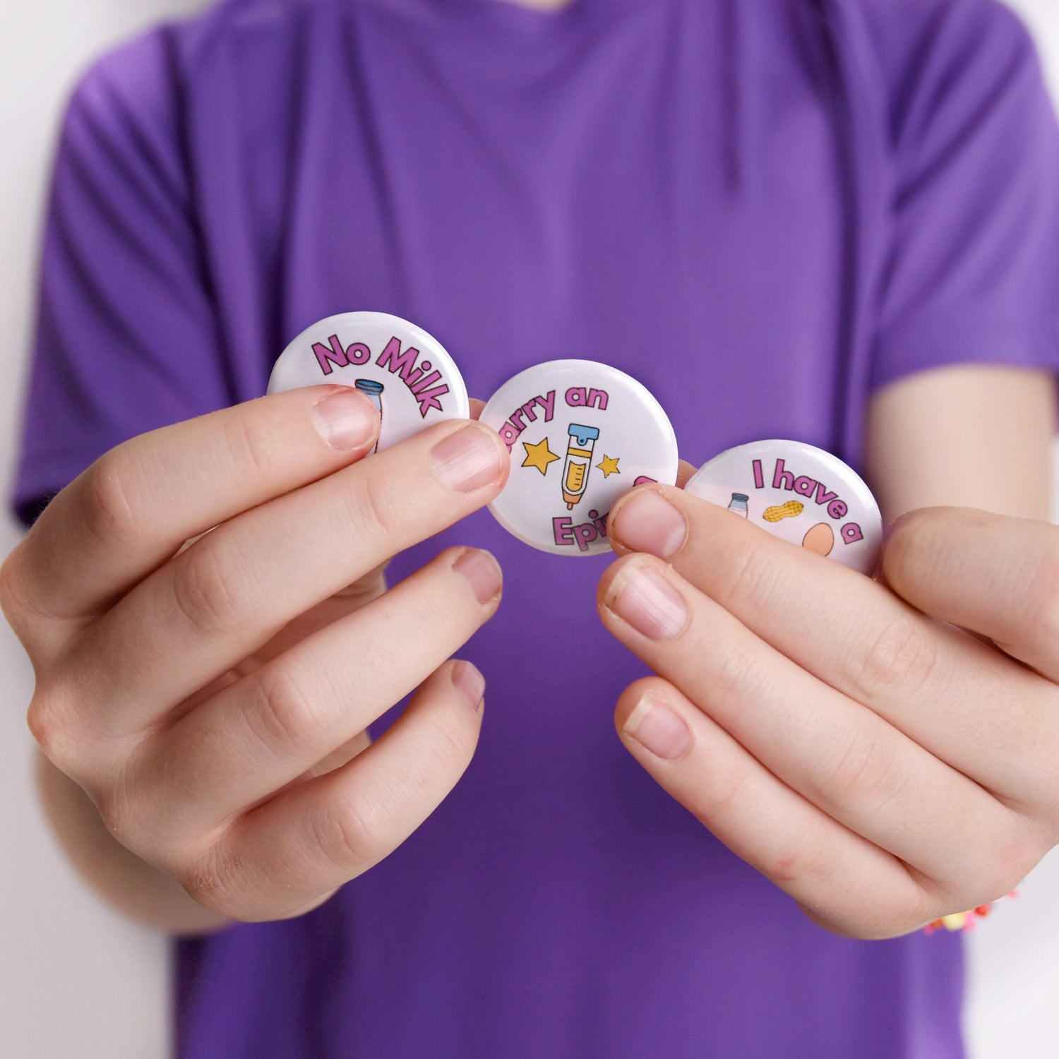 Hands holding small round badges with text and graphics against a purple shirt background