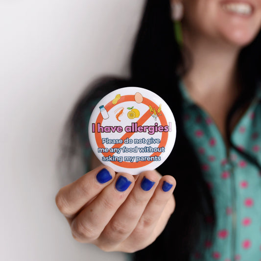 Person holding a round allergy awareness sticker with text and symbols.