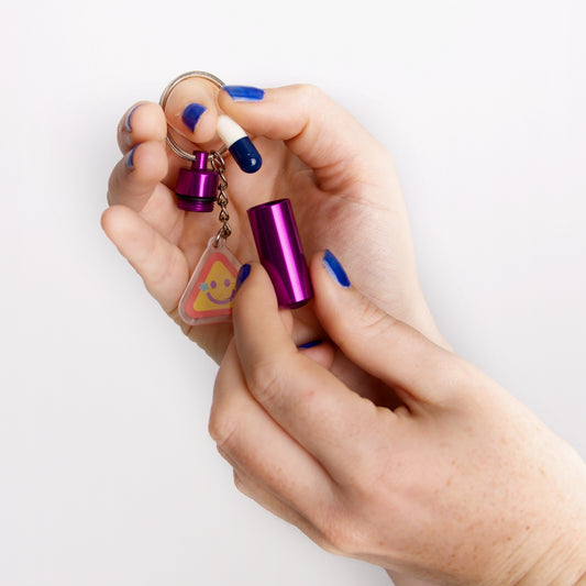 Hand holding a small purple bottle with a keychain and triangle-shaped charm on a white background