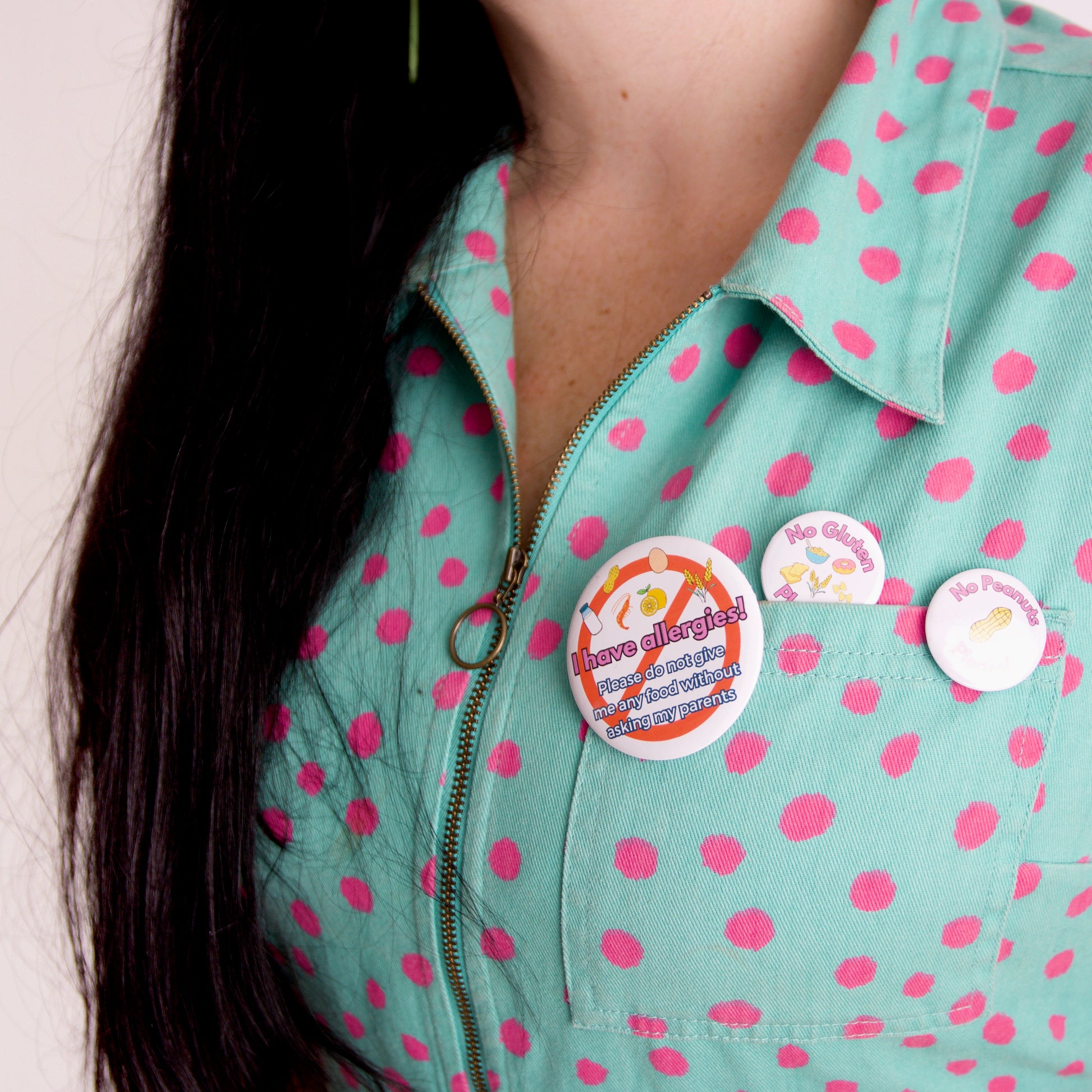 Person wearing a teal jacket with pink polka dots and multiple allergy awareness buttons.