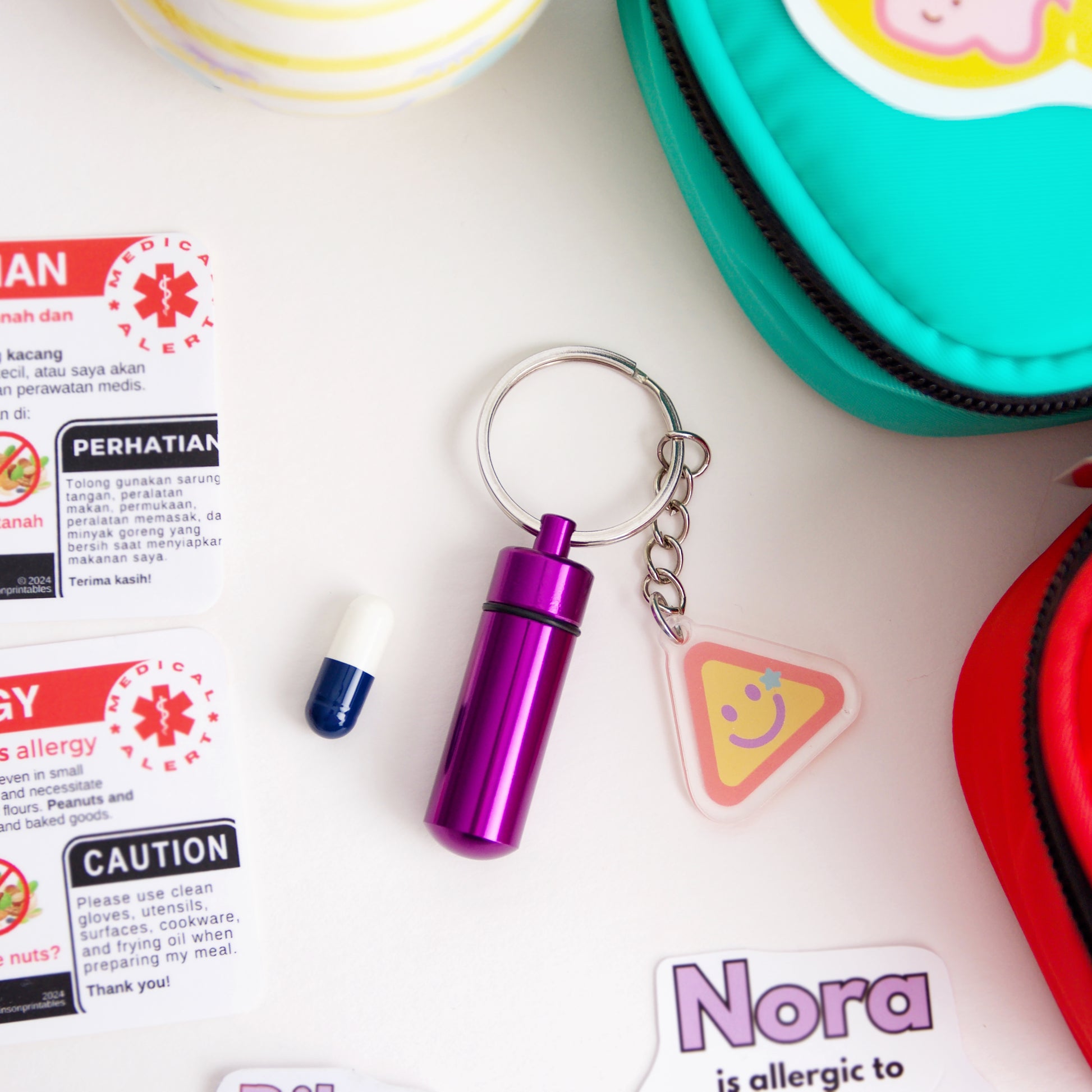 Purple keychain with a small container, surrounded by allergy alert cards and a colourful container.